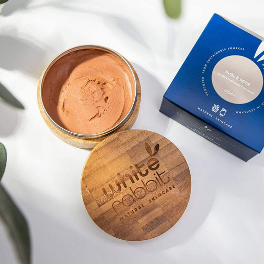 Open jar of natural skincare product with wooden lid and 'White Rabbit' branding, next to a blue box on a light background.
