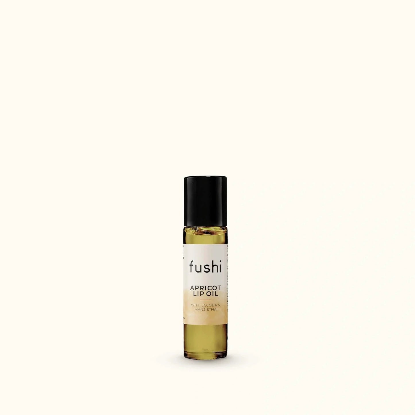A small bottle of fushi Apricot Lip Oil with a black cap and a cream label, set against a solid off-white background.