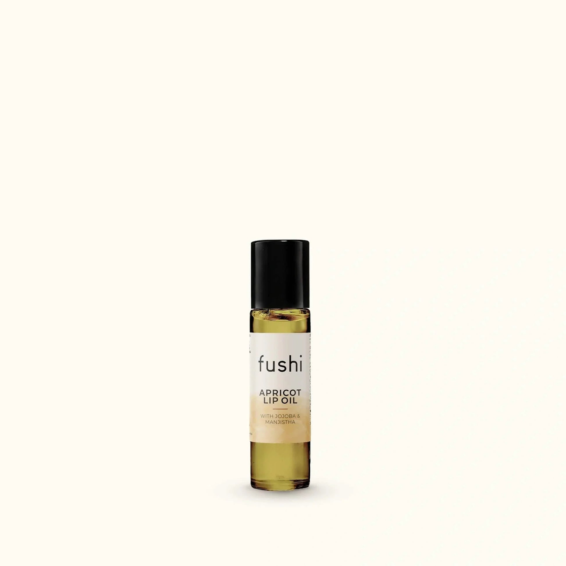 A small bottle of fushi Apricot Lip Oil with a black cap and a cream label, set against a solid off-white background.