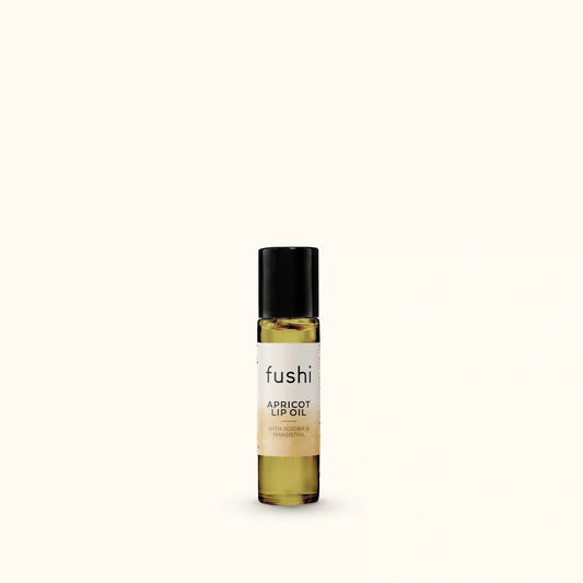 A small bottle of fushi Apricot Lip Oil with a black cap and a cream label, set against a solid off-white background.