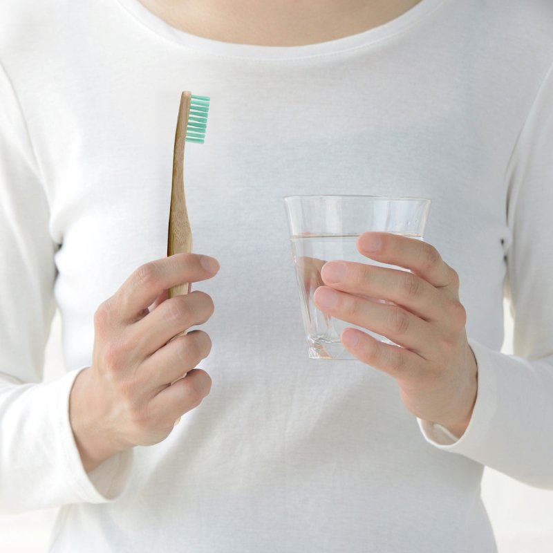 Person holding a wooden toothbrush and a glass of water against a white background