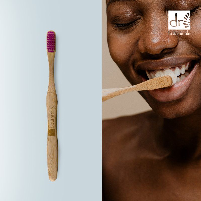 Bamboo toothbrush with purple bristles next to a person brushing their teeth, featuring Dr. Botanicals branding.