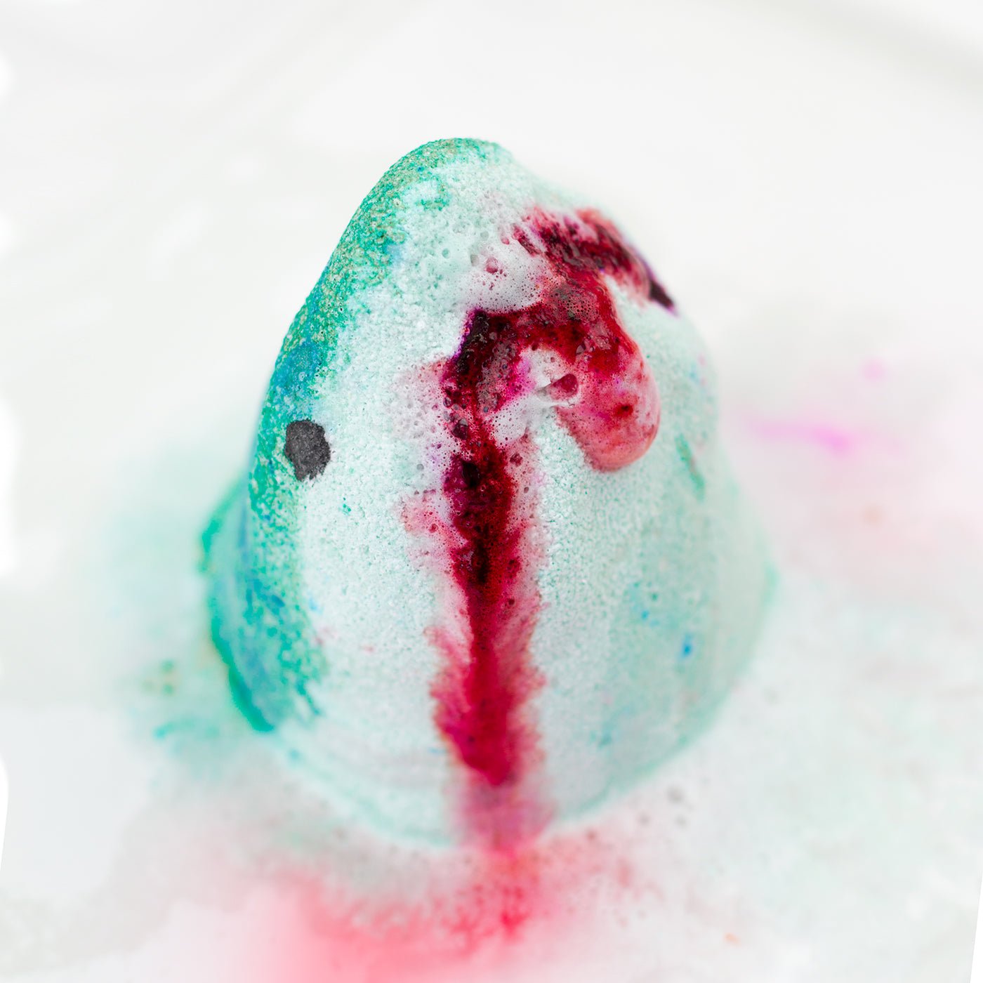 Colourful bath bomb with swirling red and green patterns on a white background