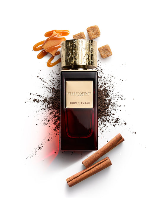 Perfume bottle labeled 'Brown Sugar' by Testament with cinnamon sticks and sugar cubes on a white background