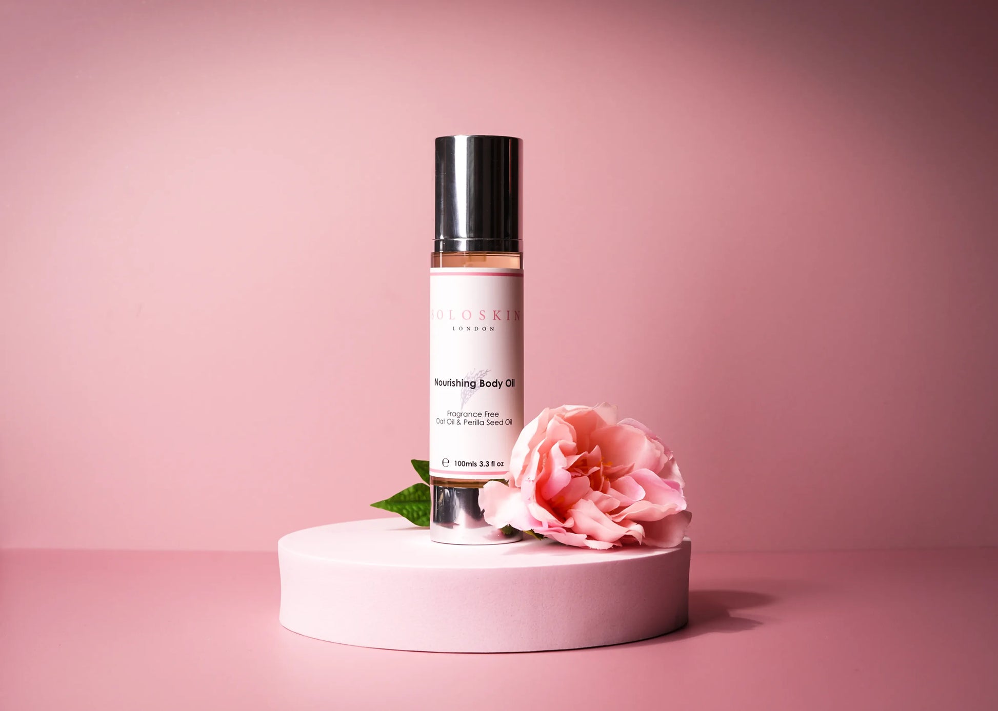 Body oil bottle with a pink flower on a pink background