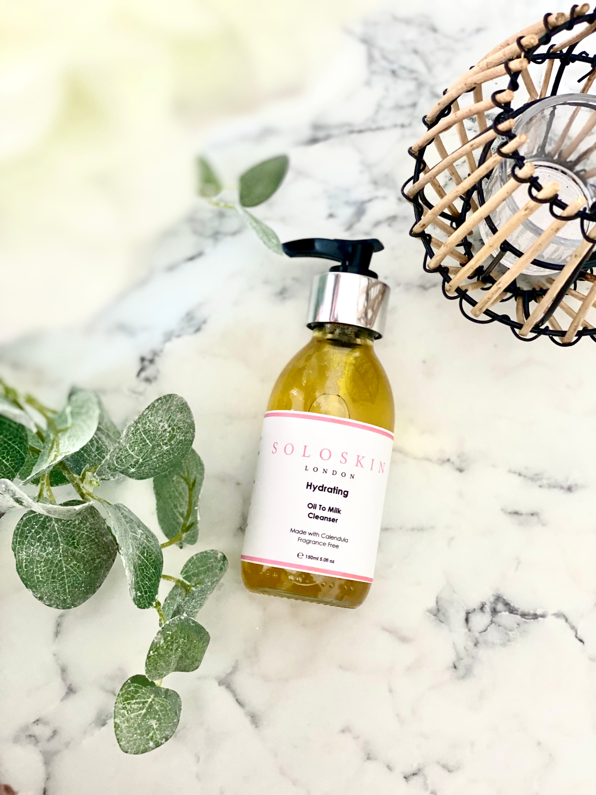 Skincare bottle with green leaves on a marble surface