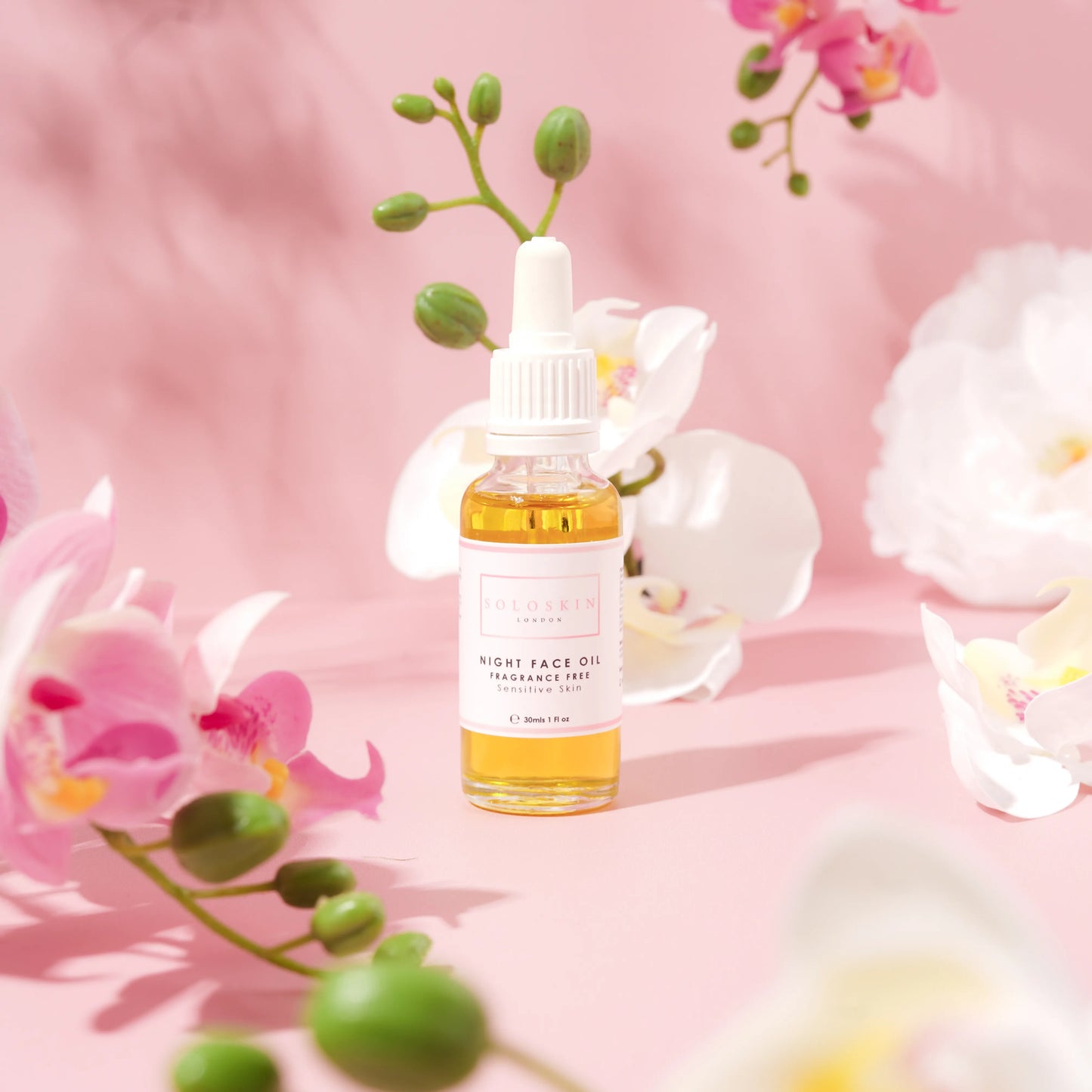 Skincare oil bottle with flowers on a pink background