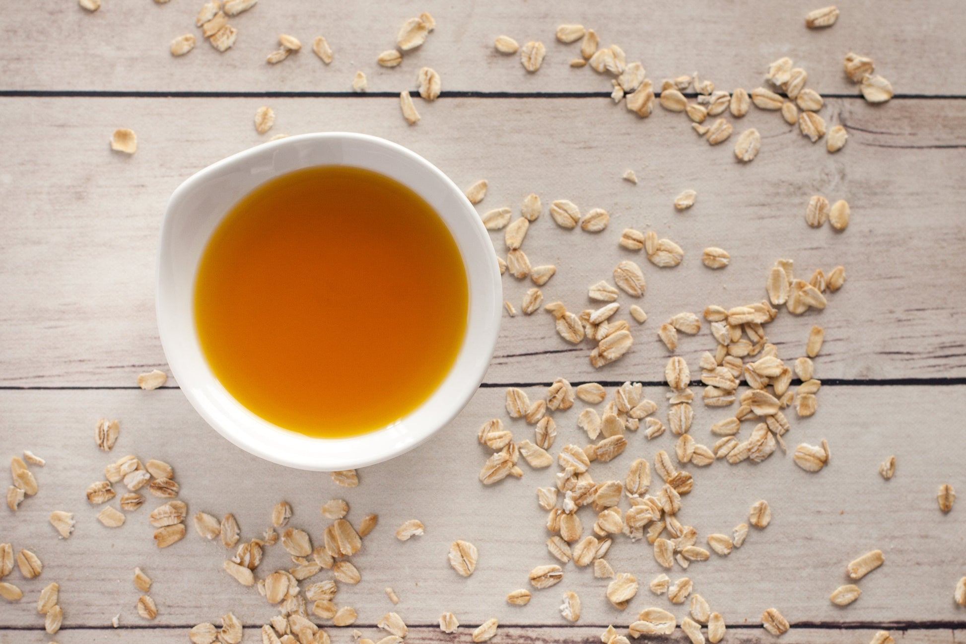 White bowl with honey surrounded by scattered oats on a wooden surface