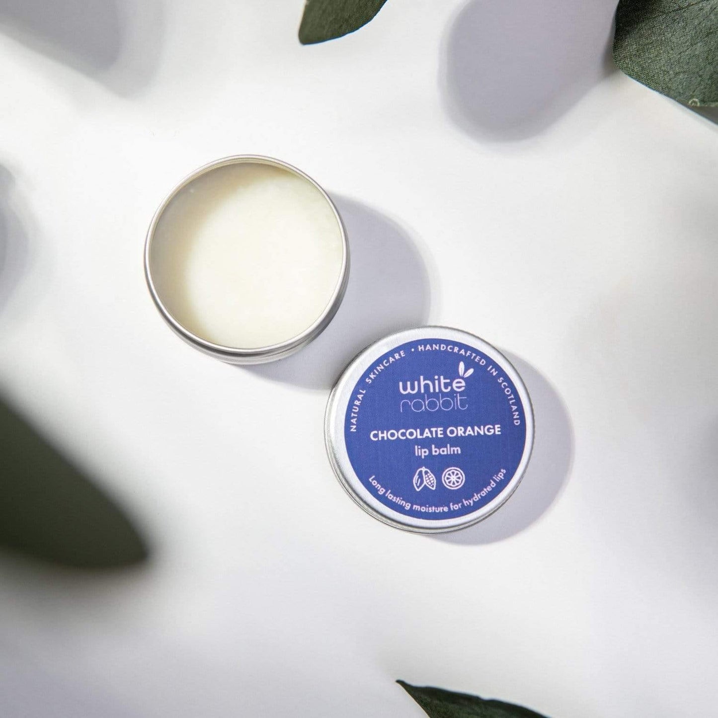 White Rabbit Chocolate Orange lip balm on a white surface with green leaves
