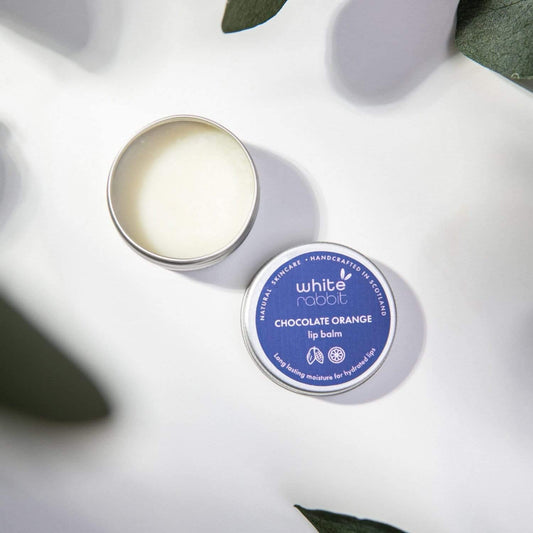 White Rabbit Chocolate Orange lip balm on a white surface with green leaves