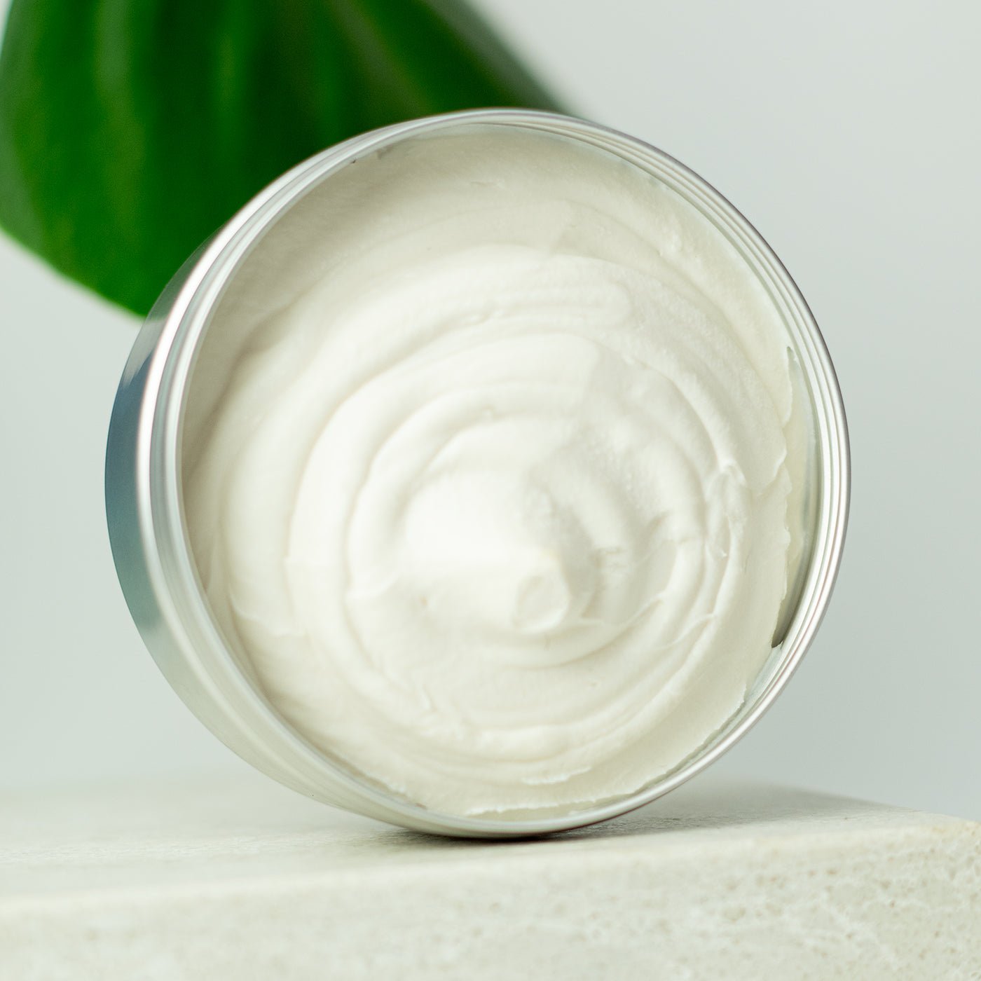 Jar of white cream with a green leaf in the background