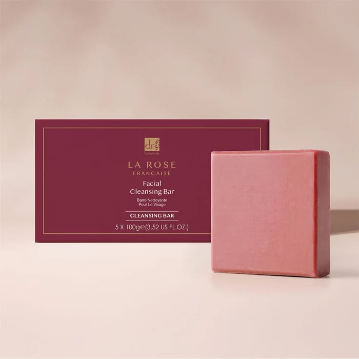 A pink rectangular facial cleansing bar soap standing in front of its deep burgundy packaging box, set against a warm beige background. The box features gold text reading 'LA ROSE FRANCAISE'.