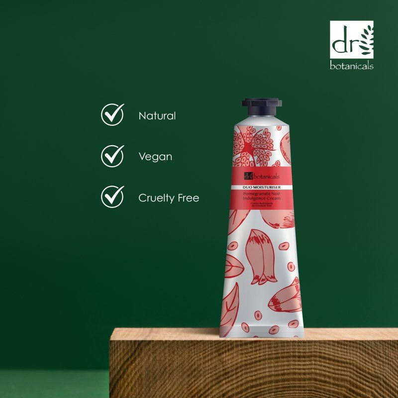 Dr Botanicals Pomegranate Noir Indulgence Cream with pomegranate design on a wooden block against a green background, featuring Dr Botanicals branding.