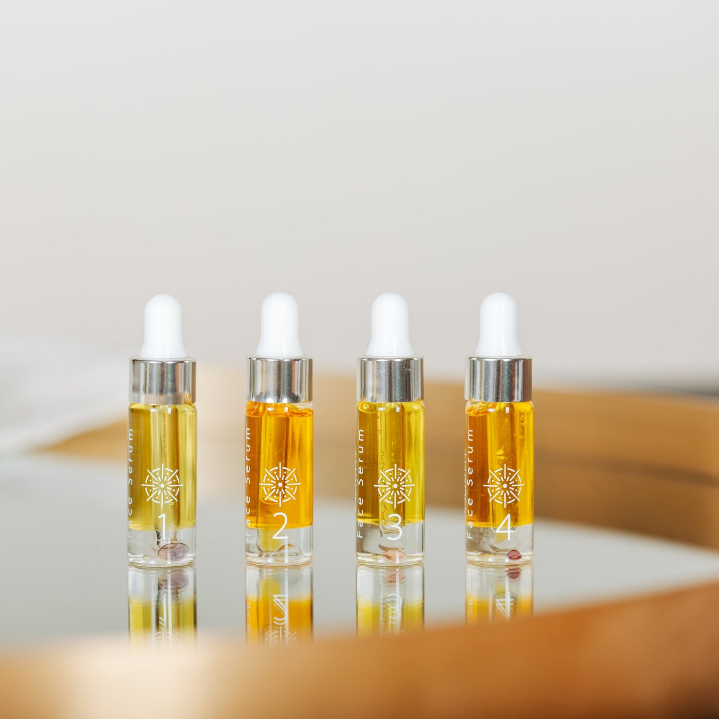 Four small clear dropper bottles filled with Inlight Beauty Supreme Face Serum 4 x 4.9ml, arranged on a reflective surface inside a round wooden tray against a soft neutral background.