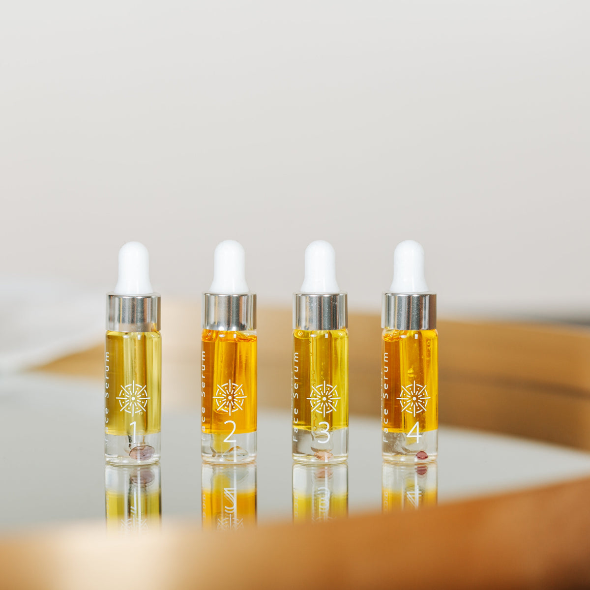 Four small clear dropper bottles filled with Inlight Beauty Supreme Face Serum 4 x 4.9ml, arranged on a reflective surface inside a round wooden tray against a soft neutral background.