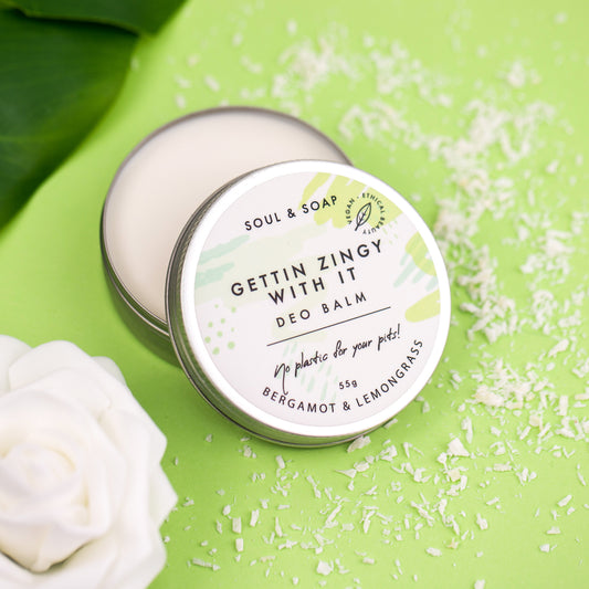 Deo balm container labeled 'Gettin Zingy With It' on a green background with white flowers and coconut shavings.