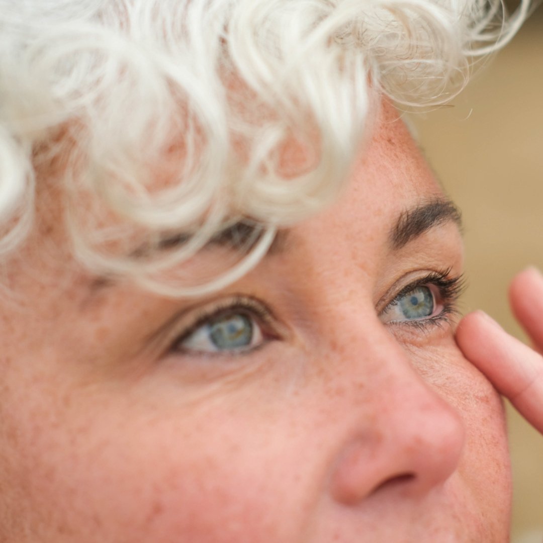 Close-up of a person with white hair and blue eyes, touching their face.