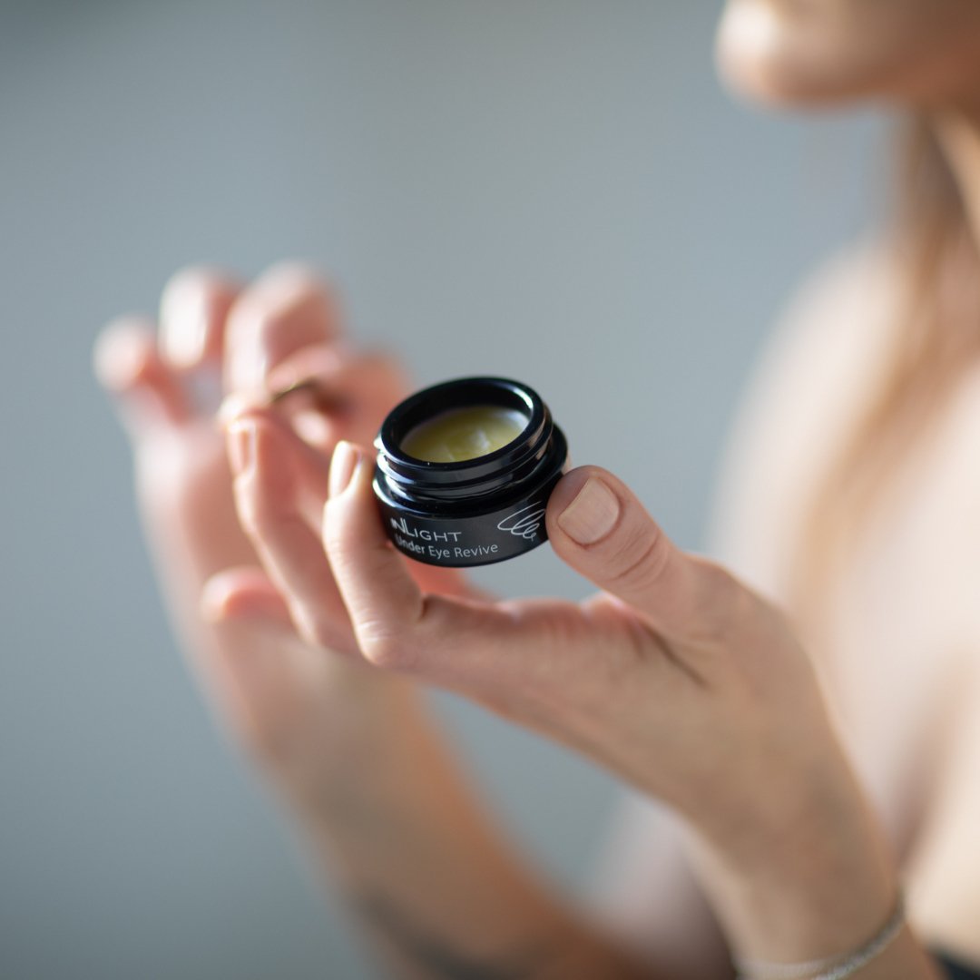 Person holding a small jar of Inlight Beauty Under Eye Revive 12ml cream with a blurred background