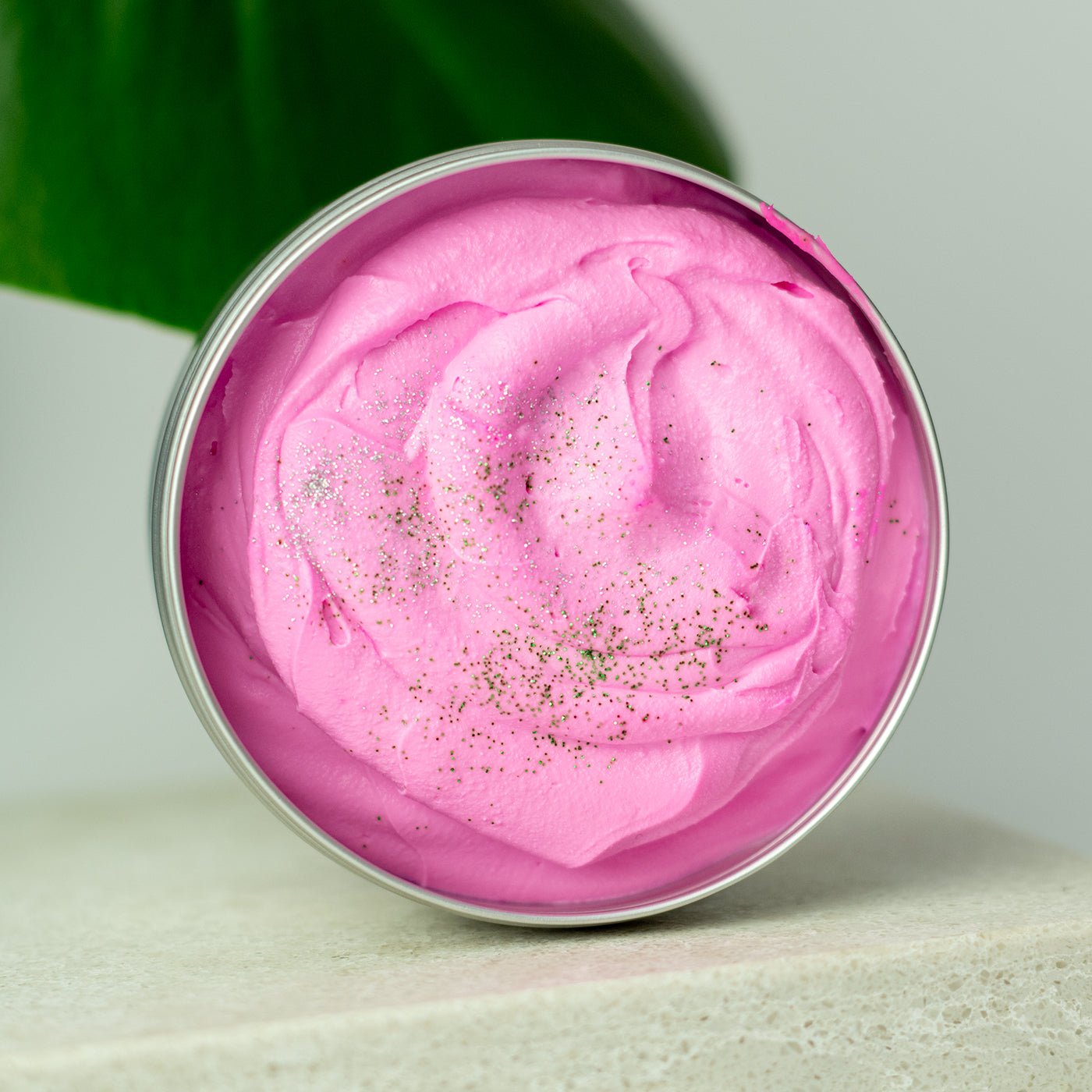 Pink whipped cream in a metal container with green leaves in the background