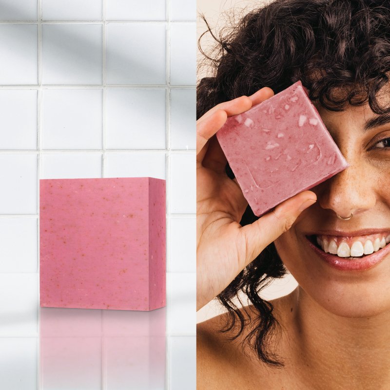 Pink soap bar with a woman holding it to her eye in a bathroom setting