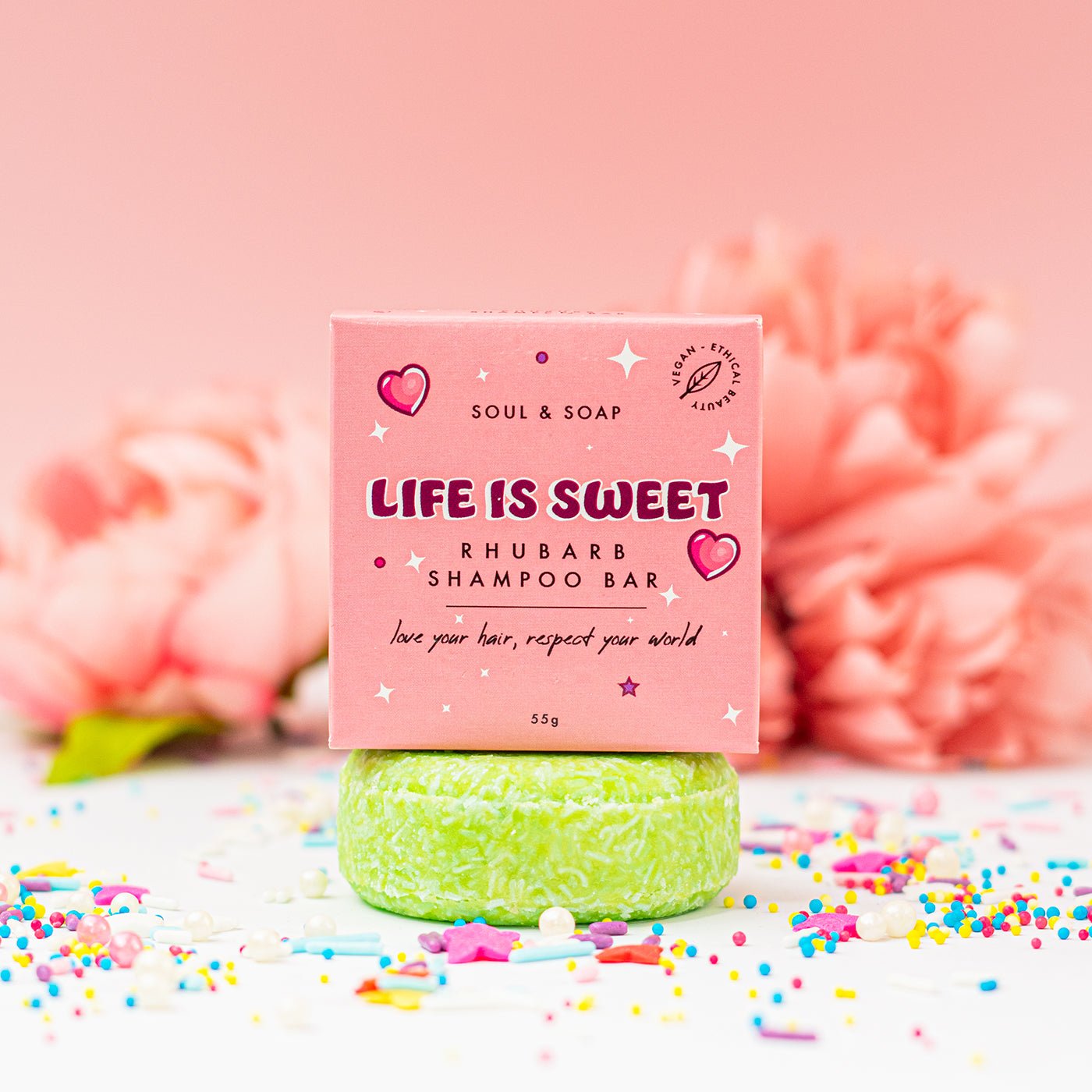 Green shampoo bar with pink packaging labeled 'Life is Sweet' on a pink background with flowers and sprinkles.