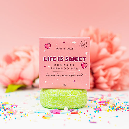Green shampoo bar with pink packaging labeled 'Life is Sweet' on a pink background with flowers and sprinkles.