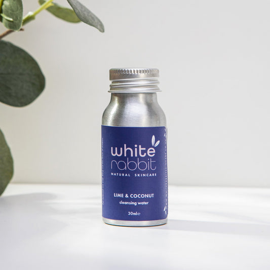 White Rabbit skincare product bottle with blue label on a white surface with green leaves in the background