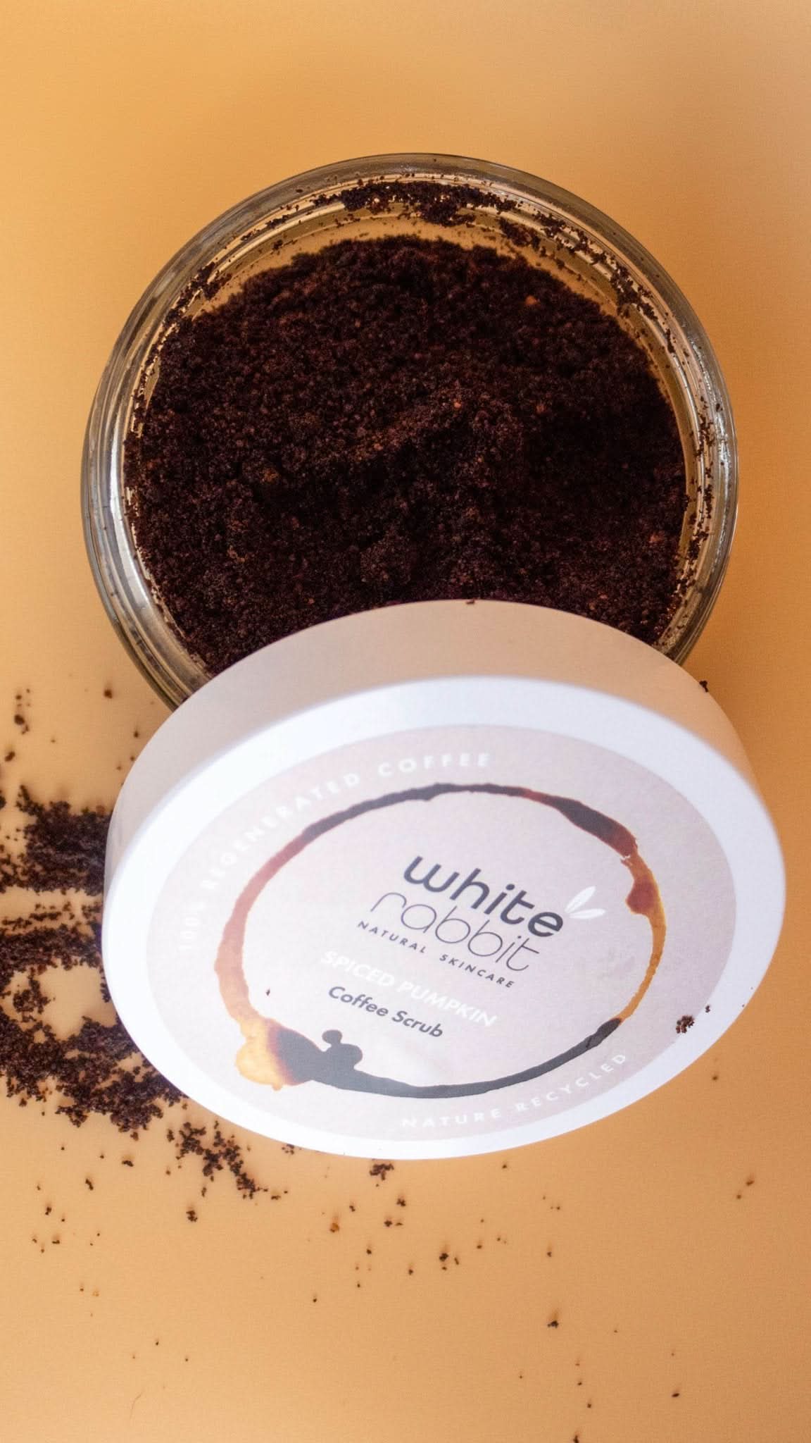 Jar of coffee scrub with a visible brand label on a beige background