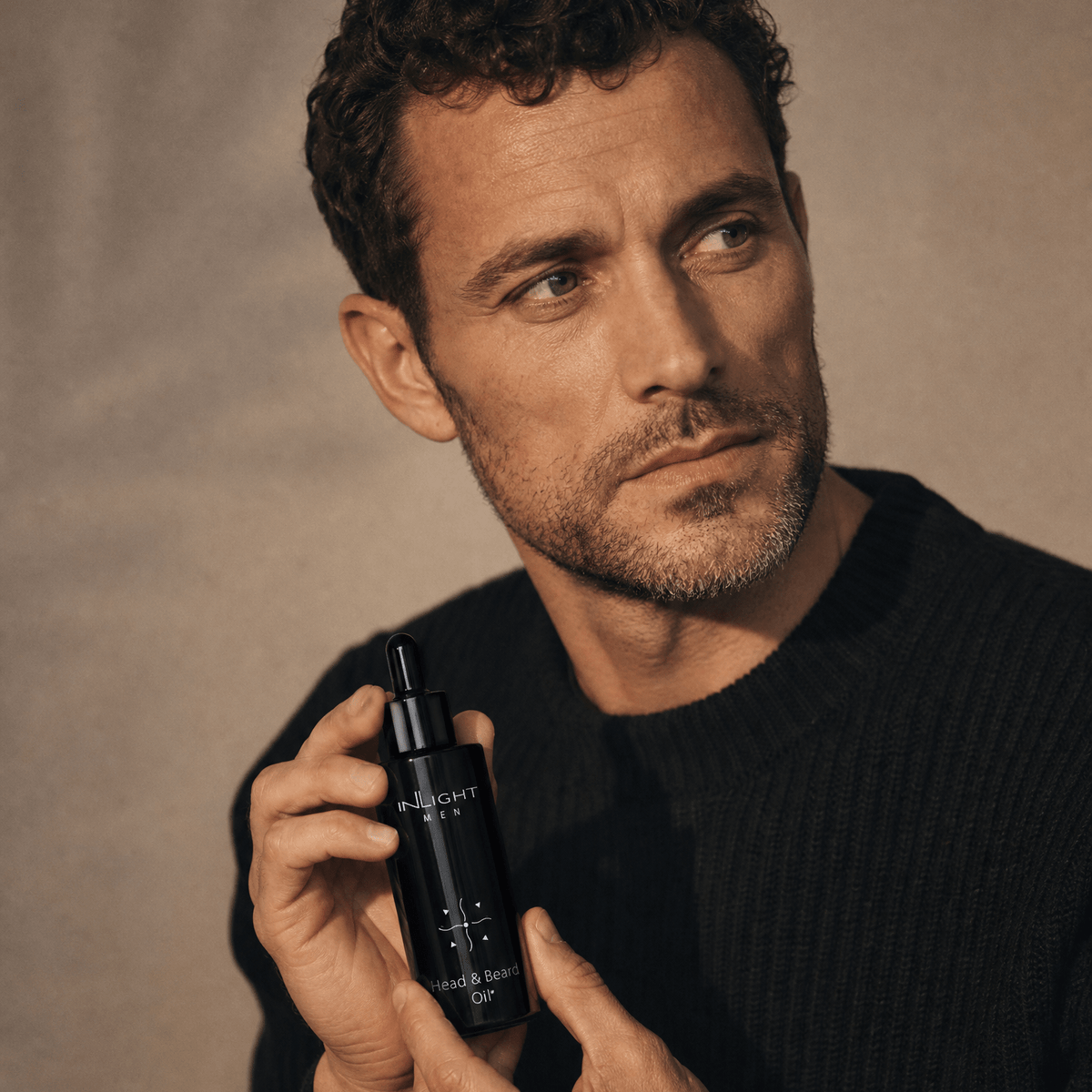 Man holding a black skincare bottle of Inlight Beauty Head & Beard Oil for Men 100ml against a neutral background