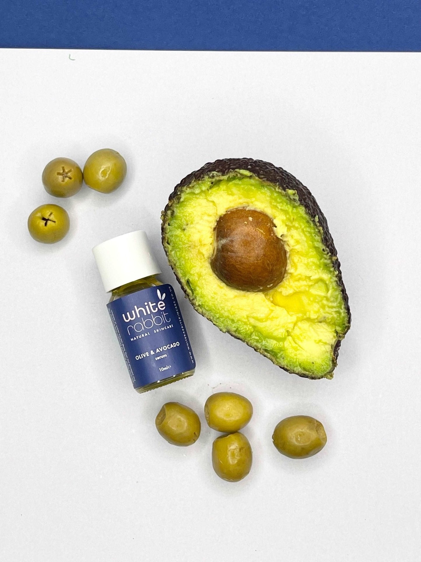 Avocado, olives, and a bottle of White Rabbit olive and avocado oil on a white background