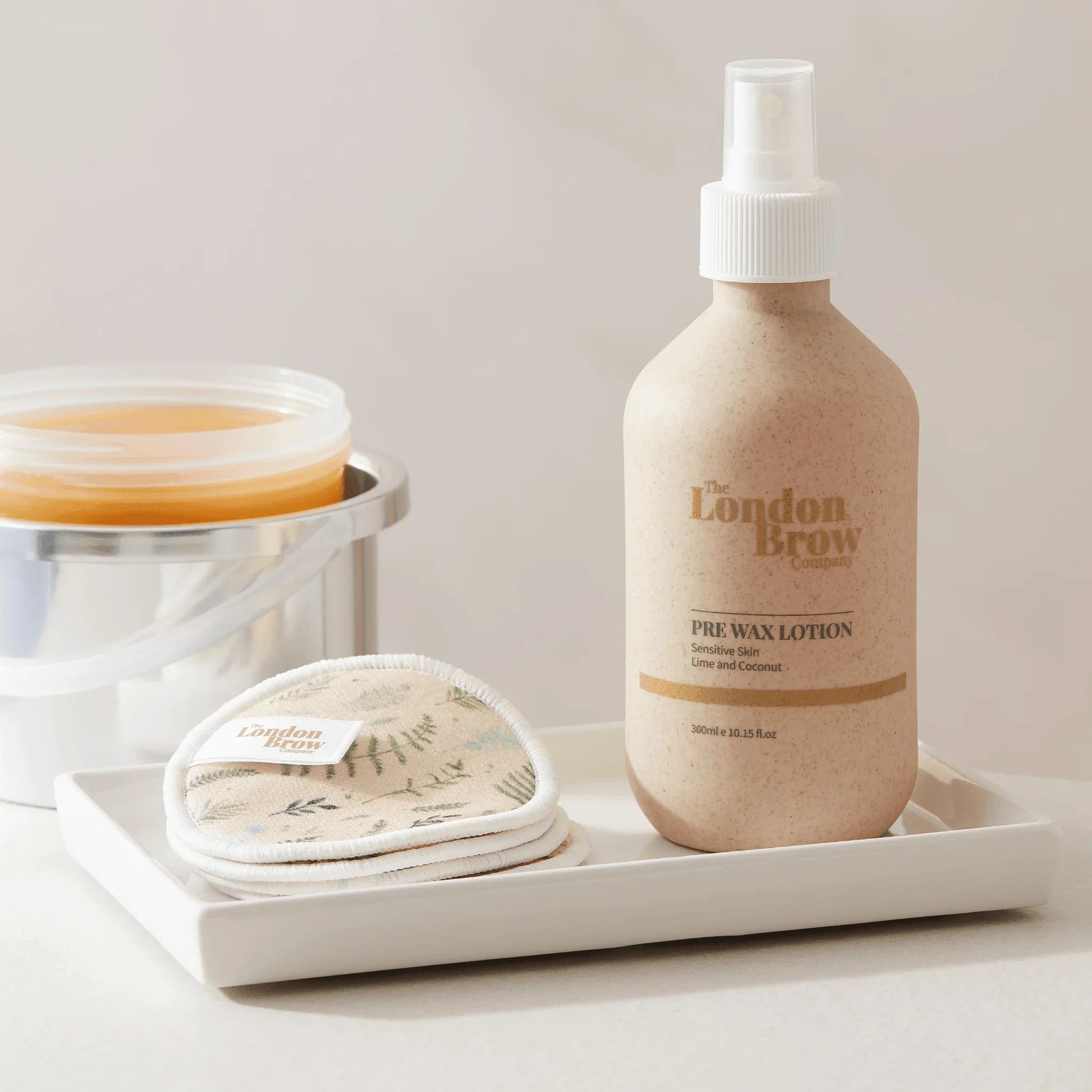 Pre-wax lotion bottle and cotton pads on a tray with a neutral background