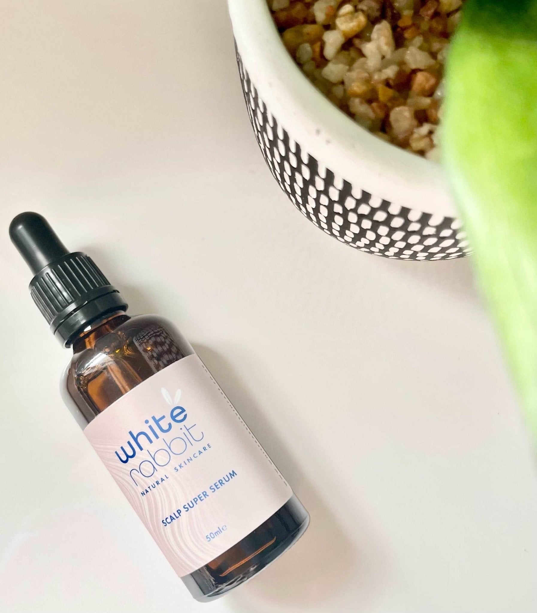 Bottle of 'White Rabbit' scalp serum on a light surface with a blurred background
