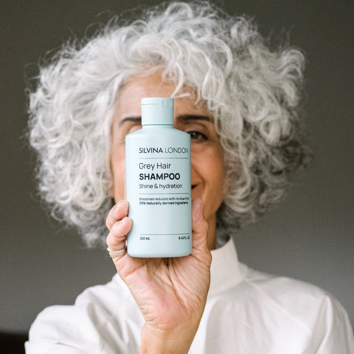 Person holding a bottle of Silvina London Grey Hair Shampoo with a neutral background