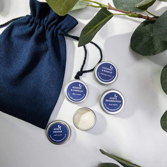 Set of small containers with blue lids on a white surface with a navy drawstring bag and green leaves.