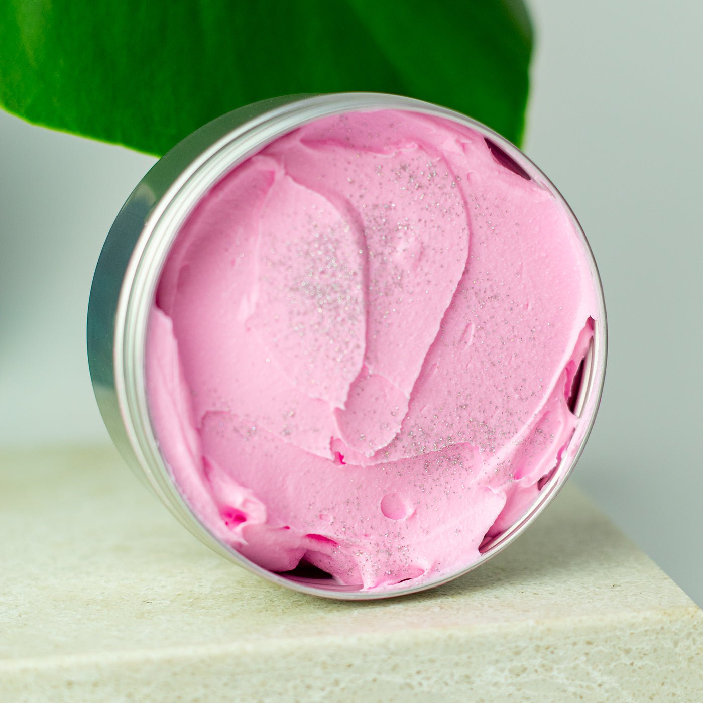 Pink cream in a silver jar with green leaves in the background