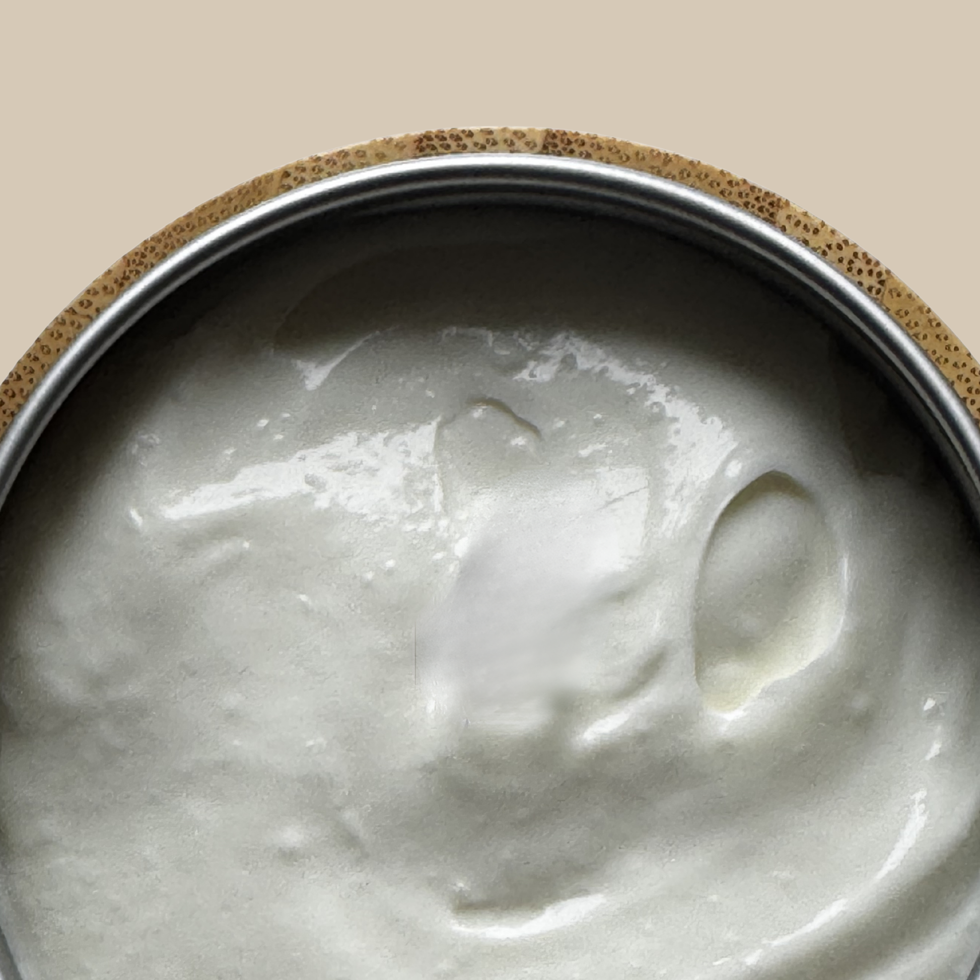 A close-up of White Rabbit Rose & Orange Night Cream 100ml inside a round container with a speckled beige rim and a silver-toned inner edge, set against a solid warm beige background.