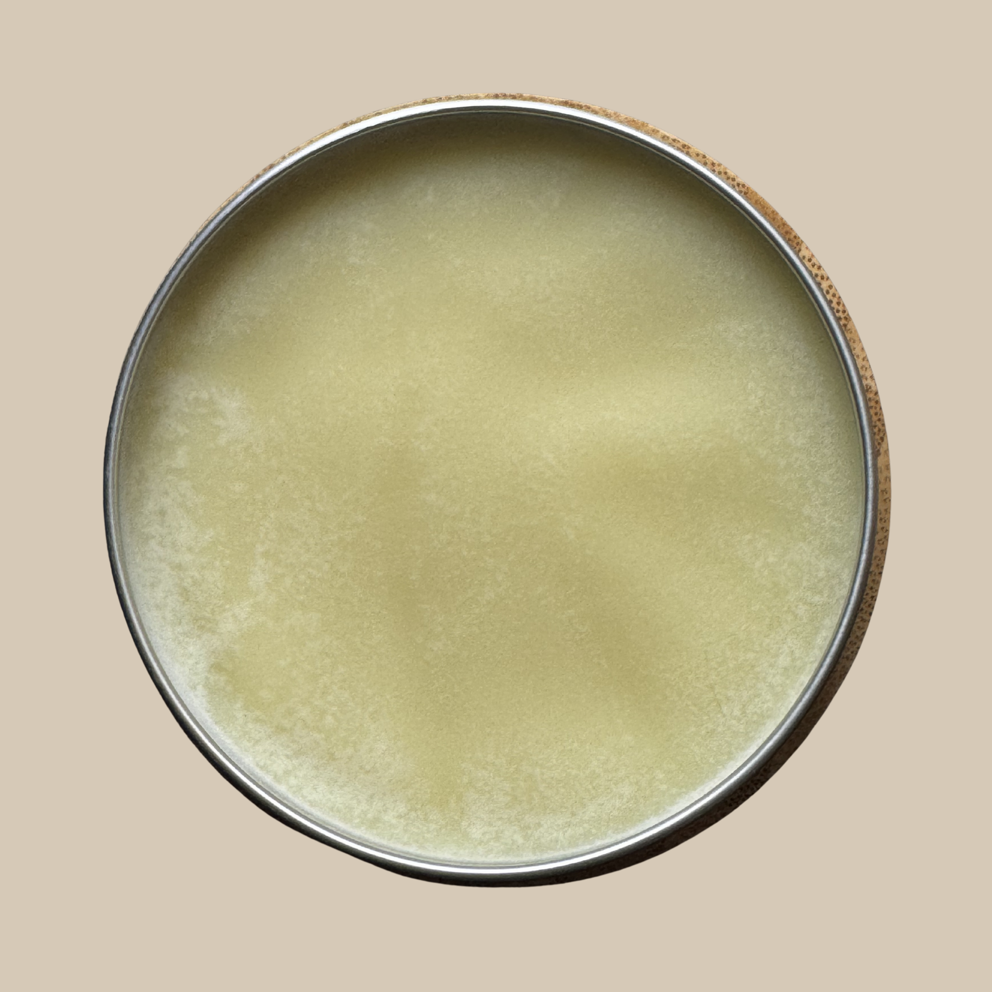A round metal tin filled with a pale yellow cream or balm, shown from above against a solid beige background.