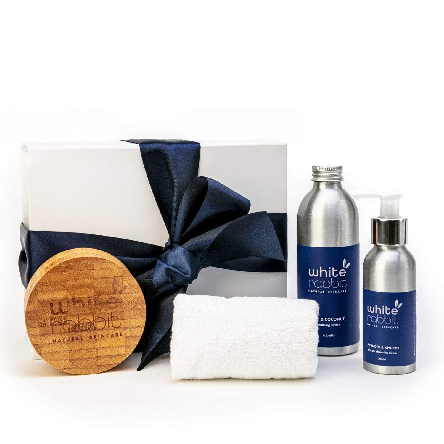 White Rabbit skincare products including bottles, a towel, and a wooden disc on a white background.