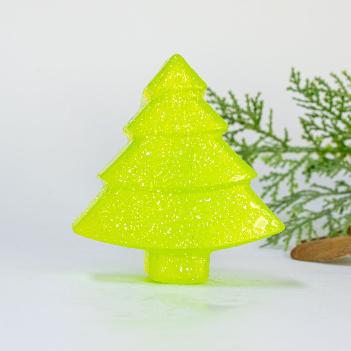 Green glittery Christmas tree-shaped soap bar on a white background with a branch in the corner.