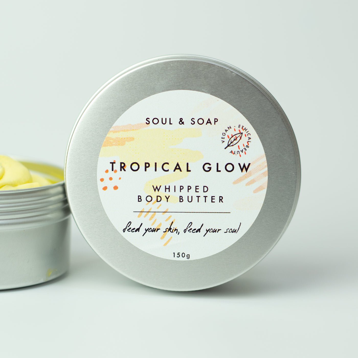 Tropical Glow whipped body butter in a silver tin with a white label on a light gray background