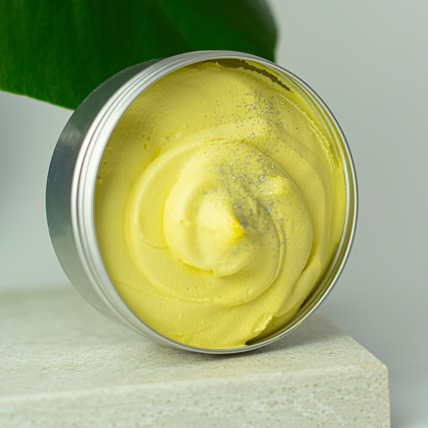 Yellow cream in a metal container on a light surface with a green leaf in the background