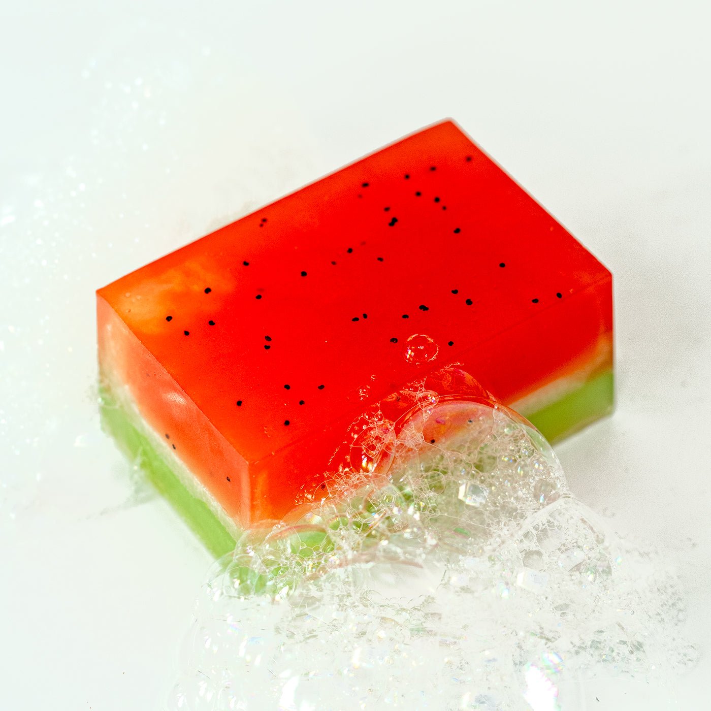 Colourful watermelon-themed soap with water droplets on a white background